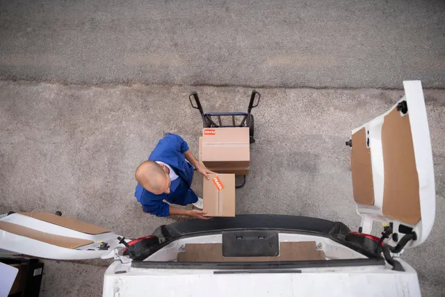 Déménageur chargeant des cartons marqués fragile dans la camionnette avec un diable